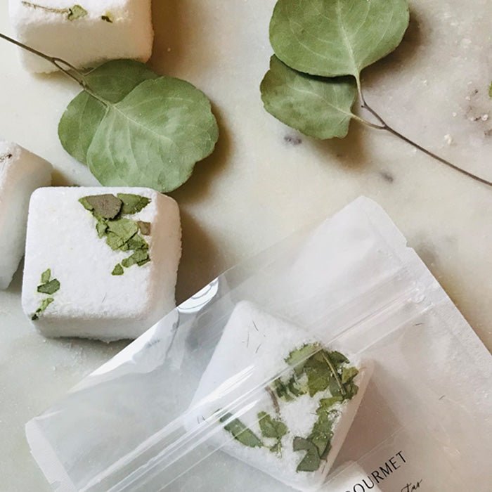 Eucalyptus leaves and white, square shower bars lying next to its translucent packaging