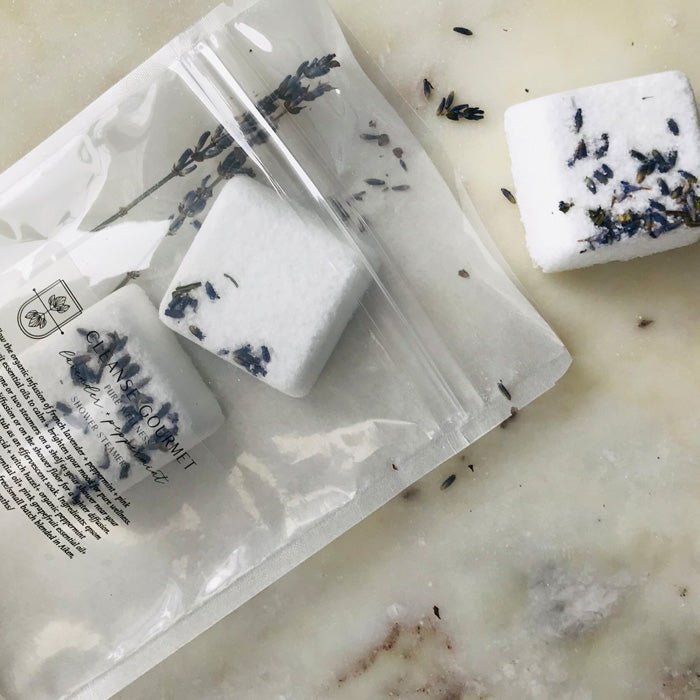 A closeup of the Lavender and Peppermint Shower Steamers, lying on a cream surface next to itheir plastic packaging.