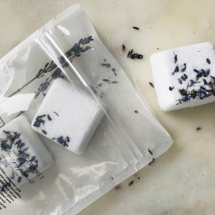 A closeup of the Lavender and Peppermint Shower Steamers, lying on a cream surface next to itheir plastic packaging.
