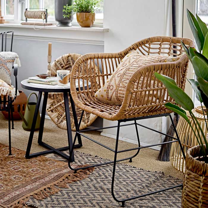 Ormelle Lounge Chair, a polyrattan lounge chair with black metal legs styled on a chevron patterned jute rug.