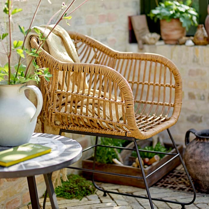 Ormelle Lounge Chair, a polyrattan lounge chair with black metal legs styled on an herringbone patio.