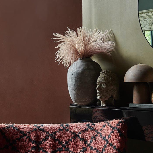 Black console with a tall grey vase, face sculpture and lamp against a rich red painted wall