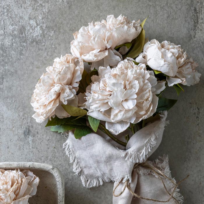 An artificial bouquet of pale pink peonies wrapped in some fabric.