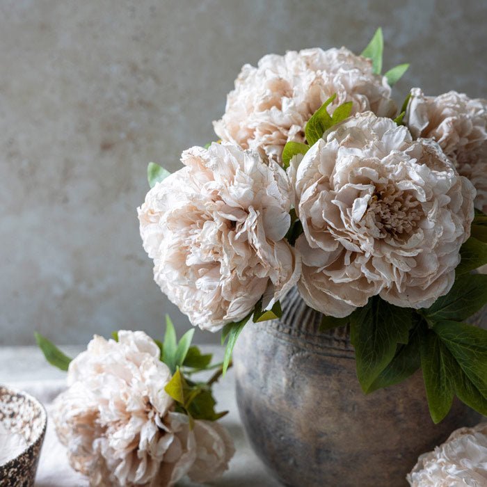 A bouquet of pale pink faux peonies in a round grey vase.