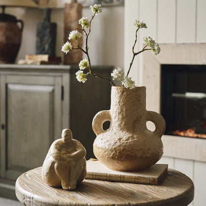 An unusual shaped vase with a wide base and two handles. Styled with a female sculpture and a sprig of blossom. Artisan style vase for a natural home.