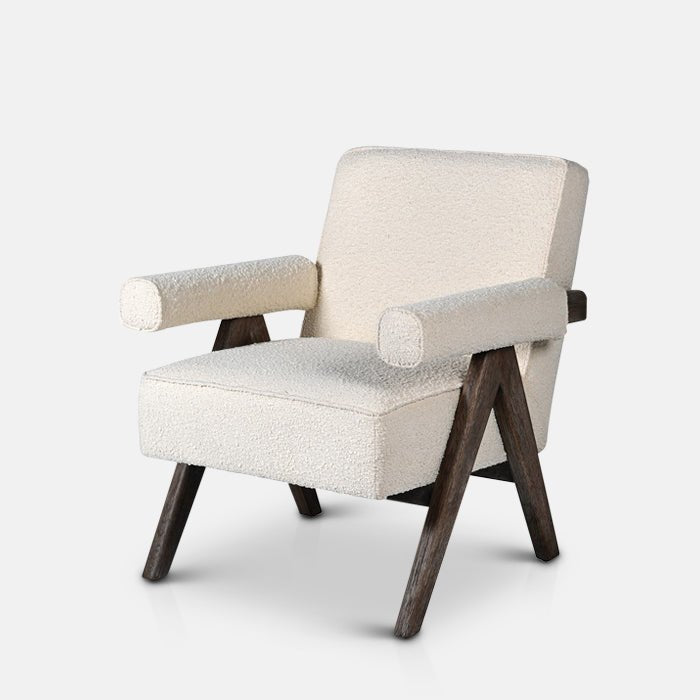 The Realta Cream Boucle Armchair, a dark wooden framed angular chair with a tilted seat and padded armrests in cream boucle.