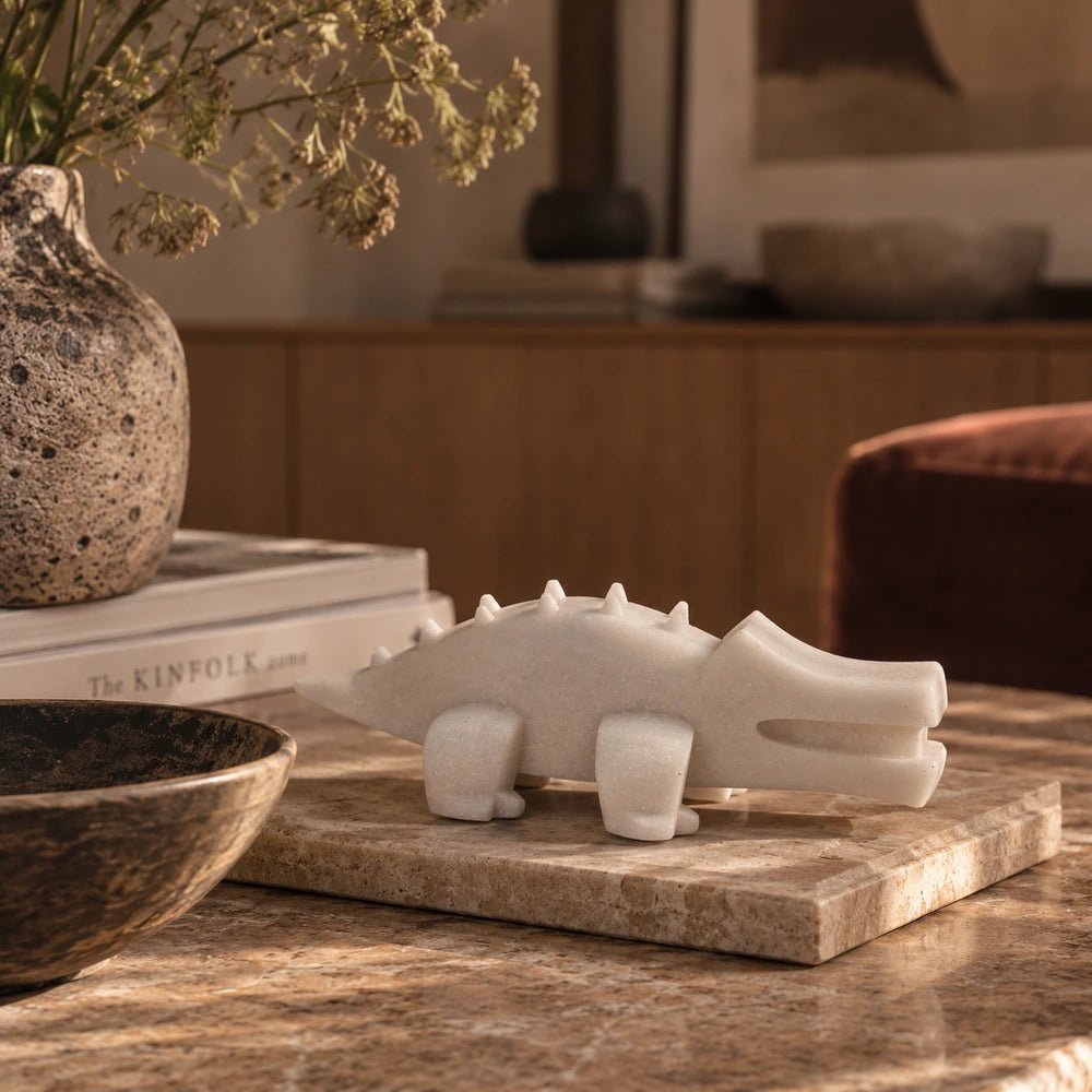 Salto Crocodile Sculpture displayed on a pale stone coffee table among stacked books, bowls and foliage, adding a small sculptural detail to a warm interior.