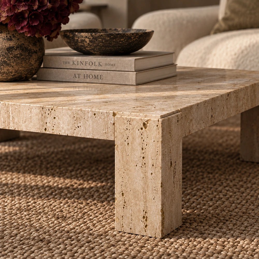 Santa Travertine Coffee Table with chunky pale stone construction, styled in a warm living room with textured rug, neutral seating, books and decorative ceramics.
