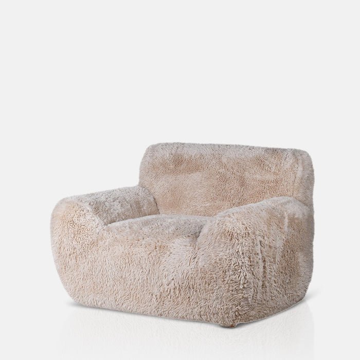 A cutout of the Saskia Armchair, an oversized armchair with a cushioned look upholstered in soft cream faux fur.