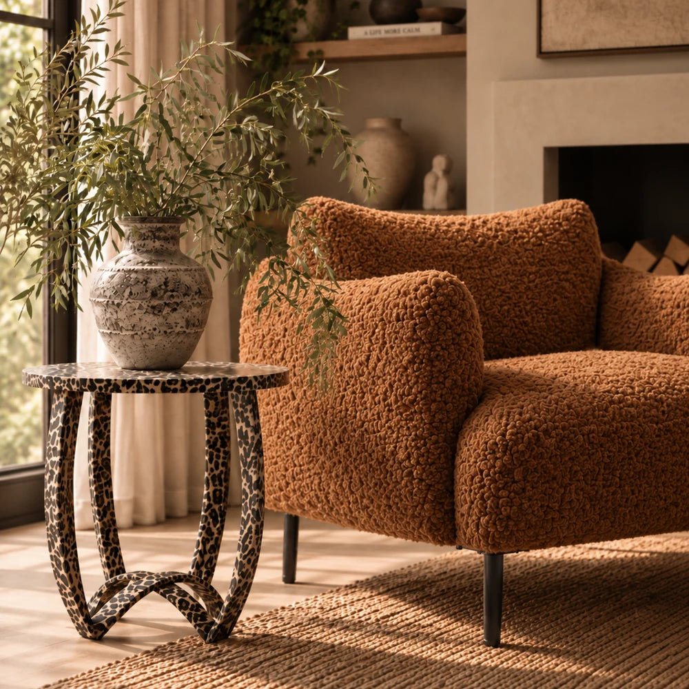 Savannah Leopard Print Side Table in a dark patterned finish, styled beside a rust boucle armchair with a decorative vase in a warm living room.