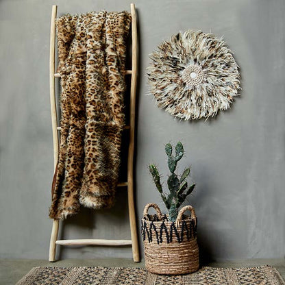 Faux fur leopard print throw folded on a wooden ladder next to a basket