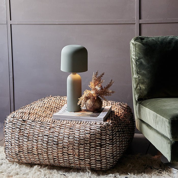 Sefton Table Lamp, a sleek matte sage metal table lamp with curved shade and smooth tapered base styled on a patterned pouf.