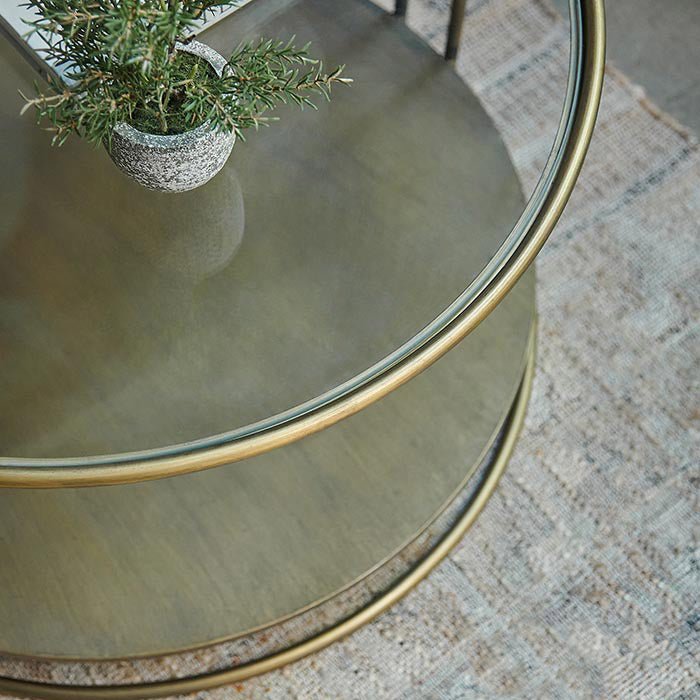 Round coffee table with brass metal frame and storage shelf, topped with clear glass.