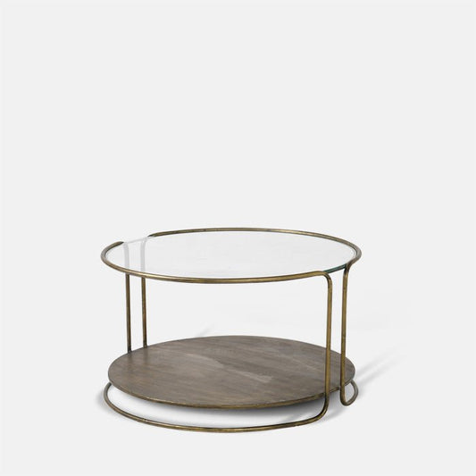 Round coffee table with clear glass top, gold metal frame, and low storage shelf.