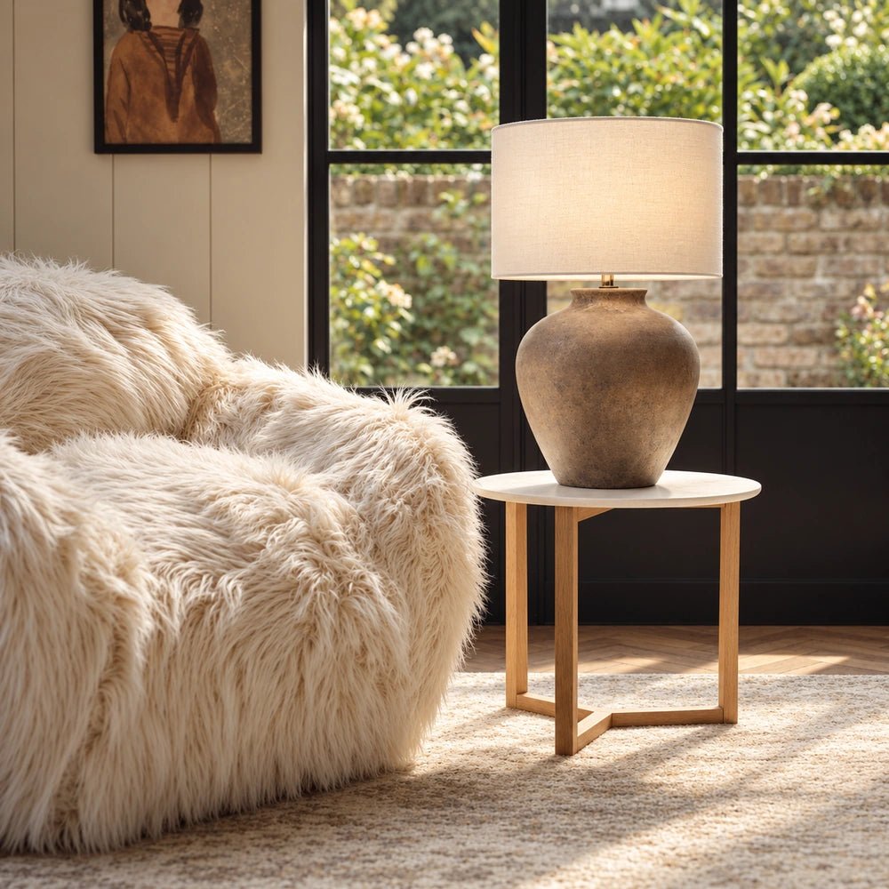 Somerdale Ceramic Table Lamp with rounded textured base and pale drum shade, styled on a wooden bedside table beside neutral bedding and decorative objects.