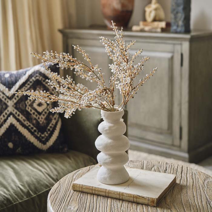 Cream unique shaped vase styled on a coffee table with some artificial flowers. Cream opaque vase in an organic shape to add a modern look to your home decor. 