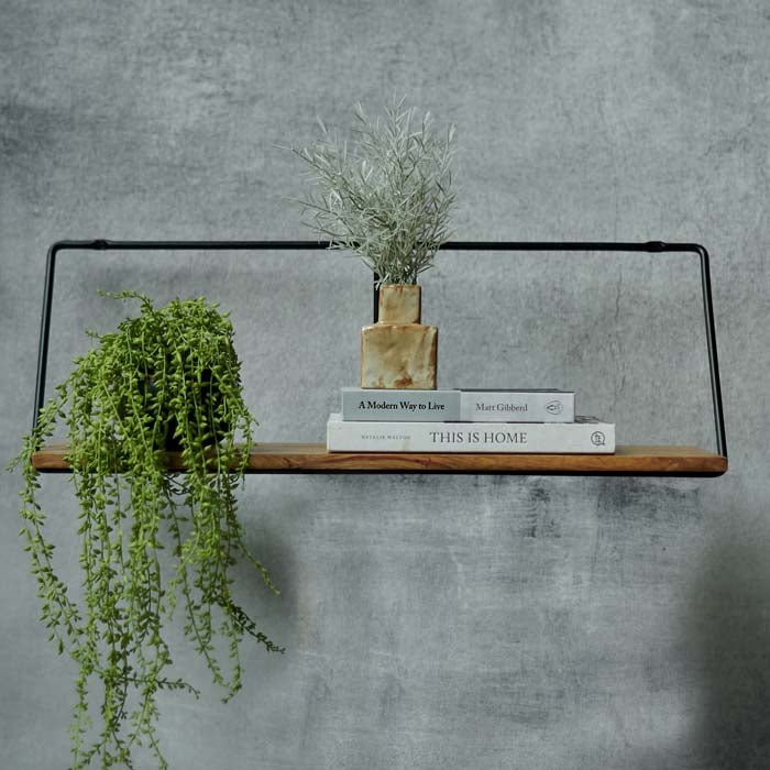 Wooden shelf sat on a black iron frame with a trailing artificial plant and vase on top