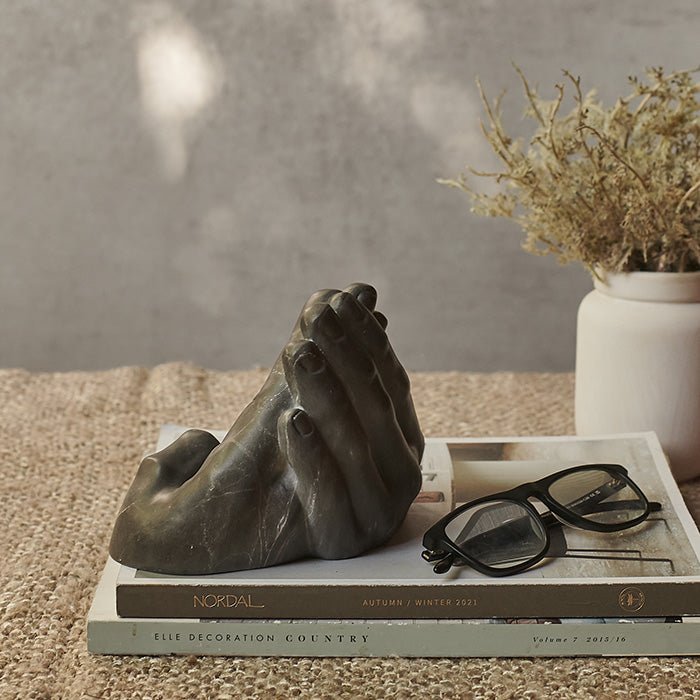 The Stony Phone Holder, a grey faux marble phone holder in the shape of two hands, sat on a book.