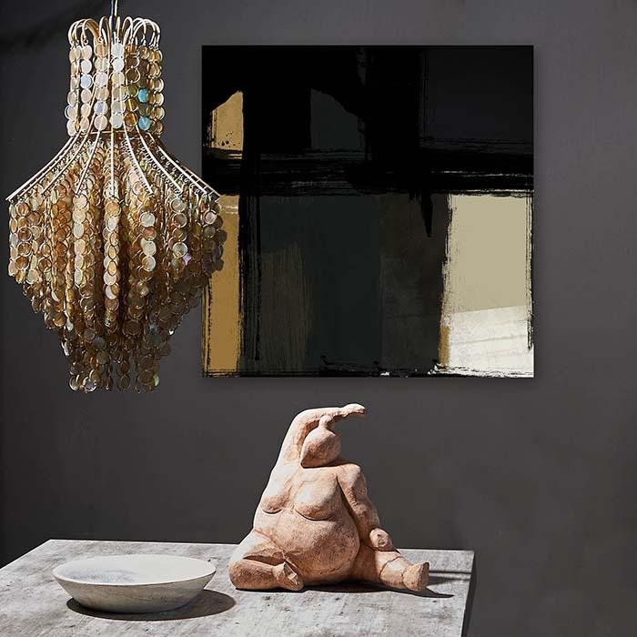 Square abstract print in yellow, grey and black hung behind a female sculpture and chandelier