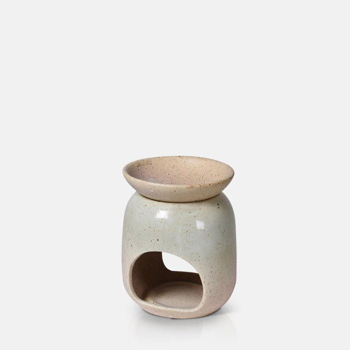 A cutout of the Thea Oil Burner, a cream coloured hourglass shaped ceramic oil burner with a brown speckled glaze.