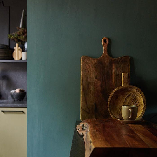 Two wooden chopping boards leaning against a dark blue wall from a black kitchen worktop