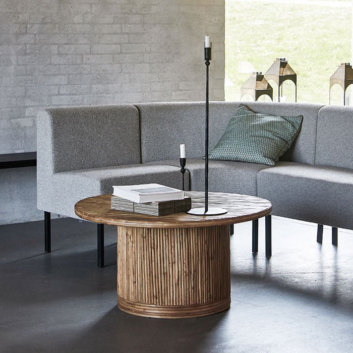 Tipton Coffee Table, a round rattan wood coffee table in warm natural brown colour next to a sofa with a green cushion.