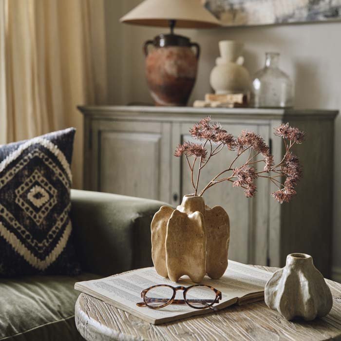 Small ceramic bud vase with an organic shape holding a flower stem on a table.