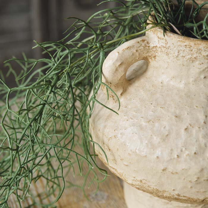 Detail image of the spiky texture of the artificial trailing asparagus fern in a beige ceramic pot.