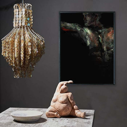 Dark rectangular framed print of a painted torso hung behind a chandelier and female sculpture