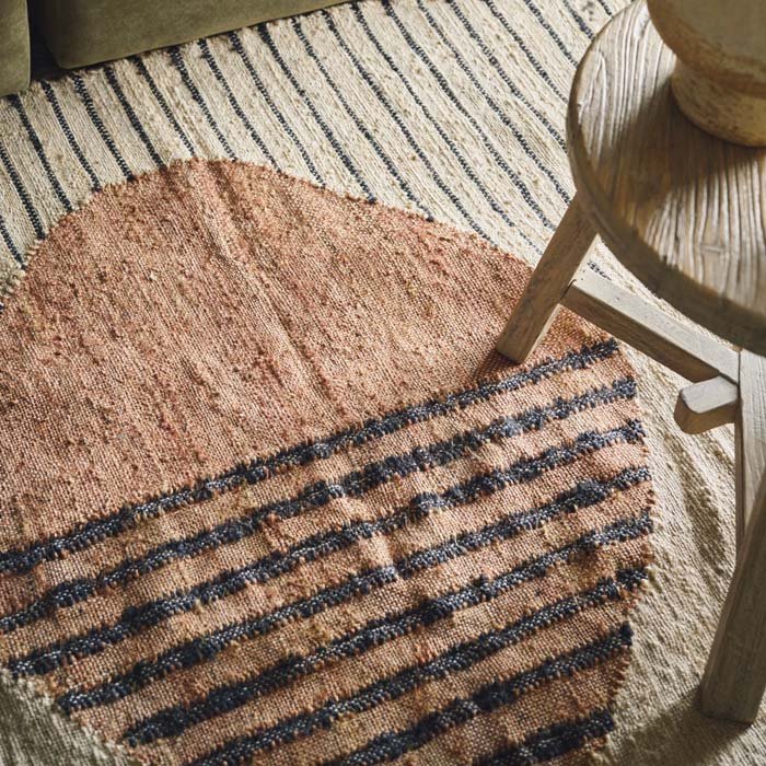 Detail of the geometric pattern on a woven jute rug, featuring a pattern with a large orange circle and perpendicular lines
