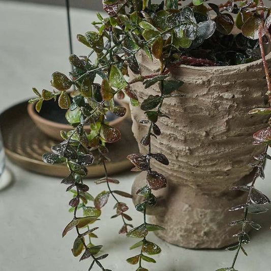 Artificial eucalyptus trailing out of a rustic stoneware vase.