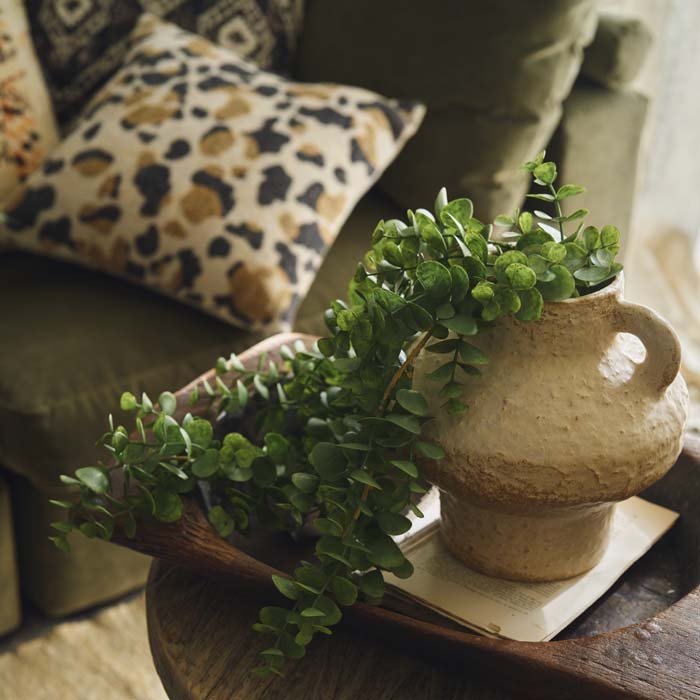 Styled image of artificial green eucalyptus coming out of a ceramic vase. Shop luxury artificial plants from interior designer Abigail Ahern.