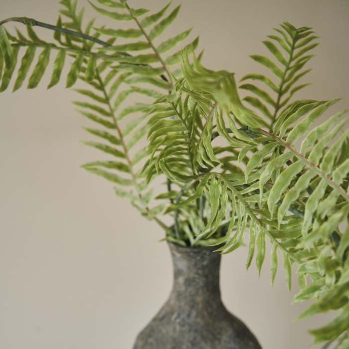Detail image of the texture on a green artificial fern in a grey vase.