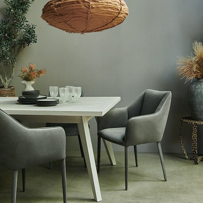 Bronson Parquet Dining Table, a rectangular herringbone wooden tiled patterned dining table styled with a set of grey chairs.