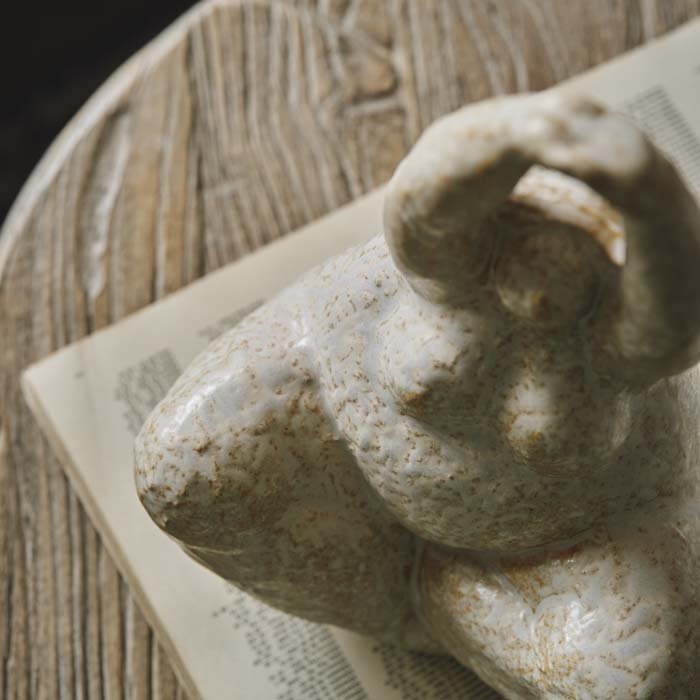 A cream ceramic sculpture of seated female yoga lady with crossed legs and her arms raised above her head style on a coffee table to create a unique vignette. 