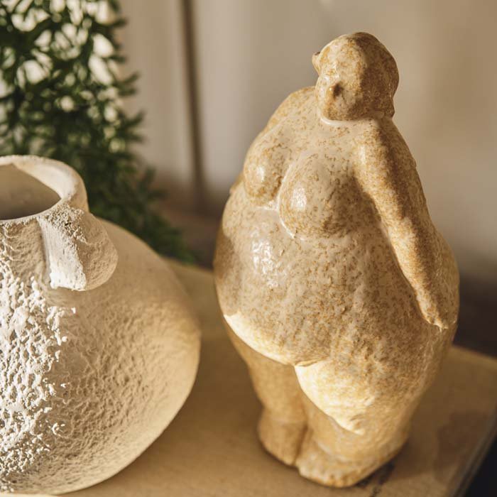 A ceramic sculpture of a curvaceous lady in a standing pose. Cream sculpture made from ceramic in a light textured glaze. Unique home accessories