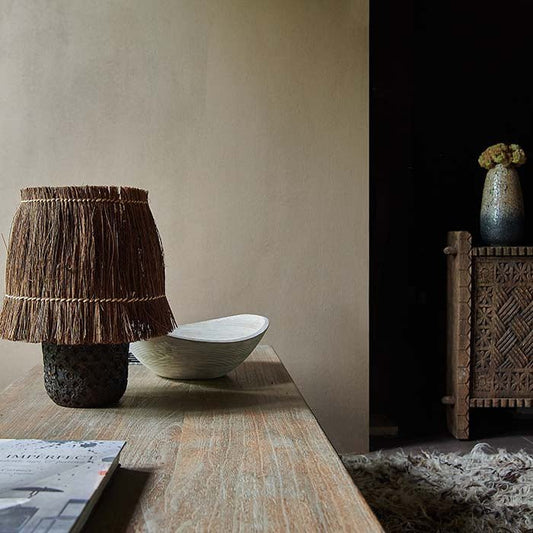 A chalky matt light coloured painted room. Earthy paint shade wattle from Abigail Ahern styled with a long wooden table with a natural brown table lamp.