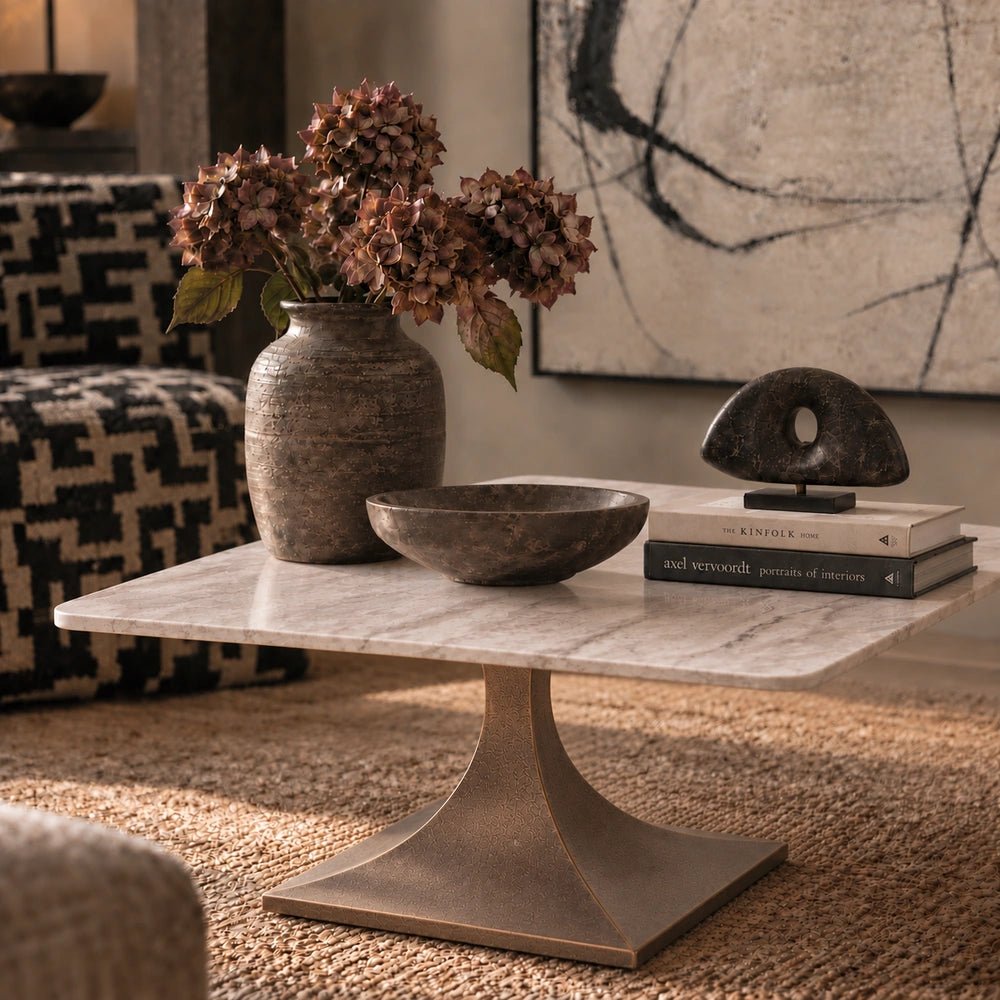 Waylon Marble Coffee Table with pale rounded stone top and sculptural pedestal base, styled with books, ceramics and flowers in a warm living room.