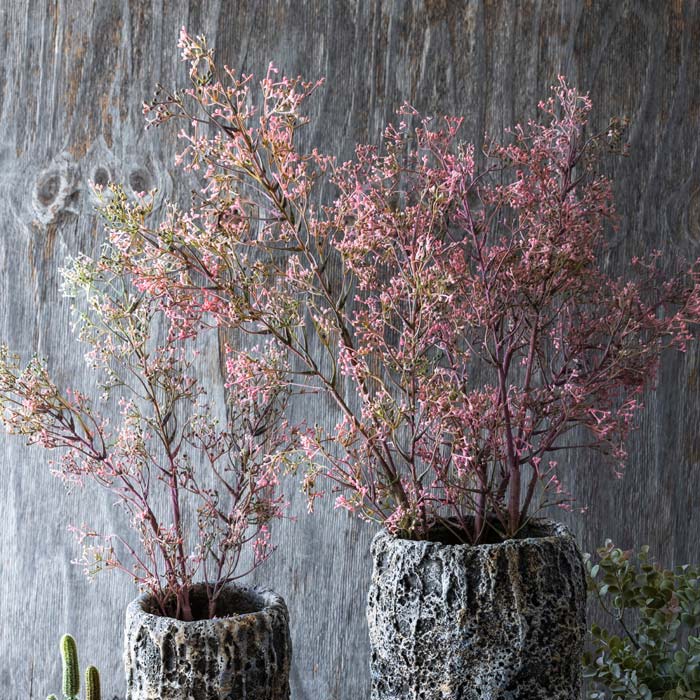 Two bouquets of tall pink artificial flower stems covered in small floral buds in grey vases.