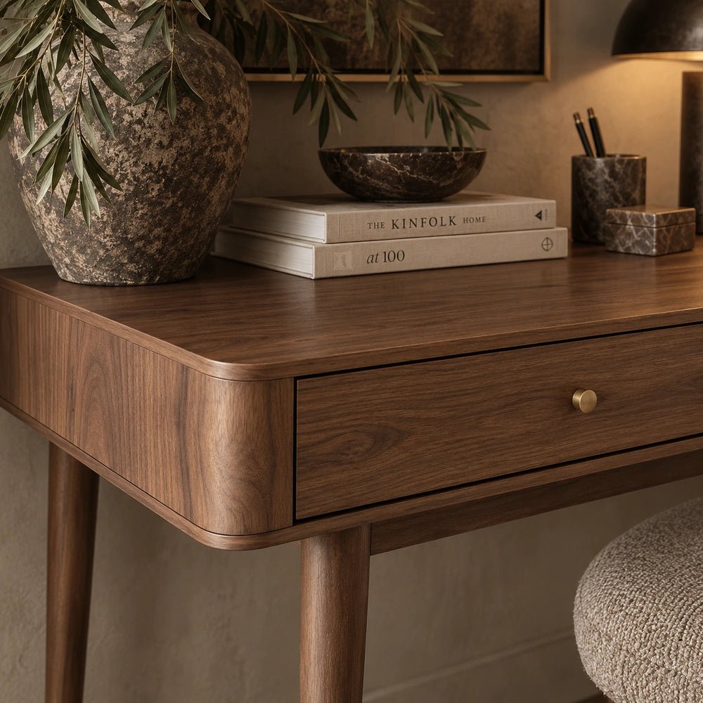 Winslow Desk with rounded dark wood desktop and single drawer, styled with books, a textured vase and desk accessories in a warm interior.
