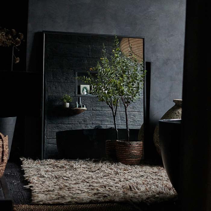 The Winston Mirror, a large rectangular mirror with a thin black frame leaning against a wall on a brown shaggy rug. 