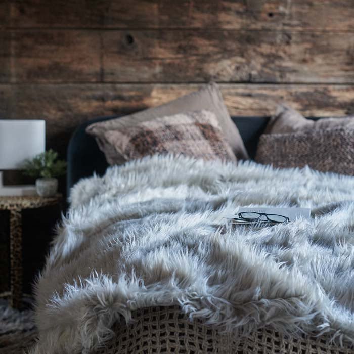 The Zea throw is a silvery grey faux fur textured throw styled across a double bed. Amazing texture and warmth against the headboard made from reclaimed wood. Styled with extra cushions and pillows.