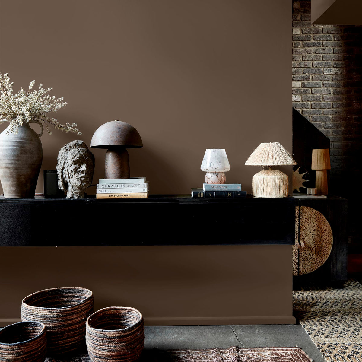 Abigail Ahern After Dawn paint – warm chocolate brown with purple undertones on living room wall with shelf, lamps and vases