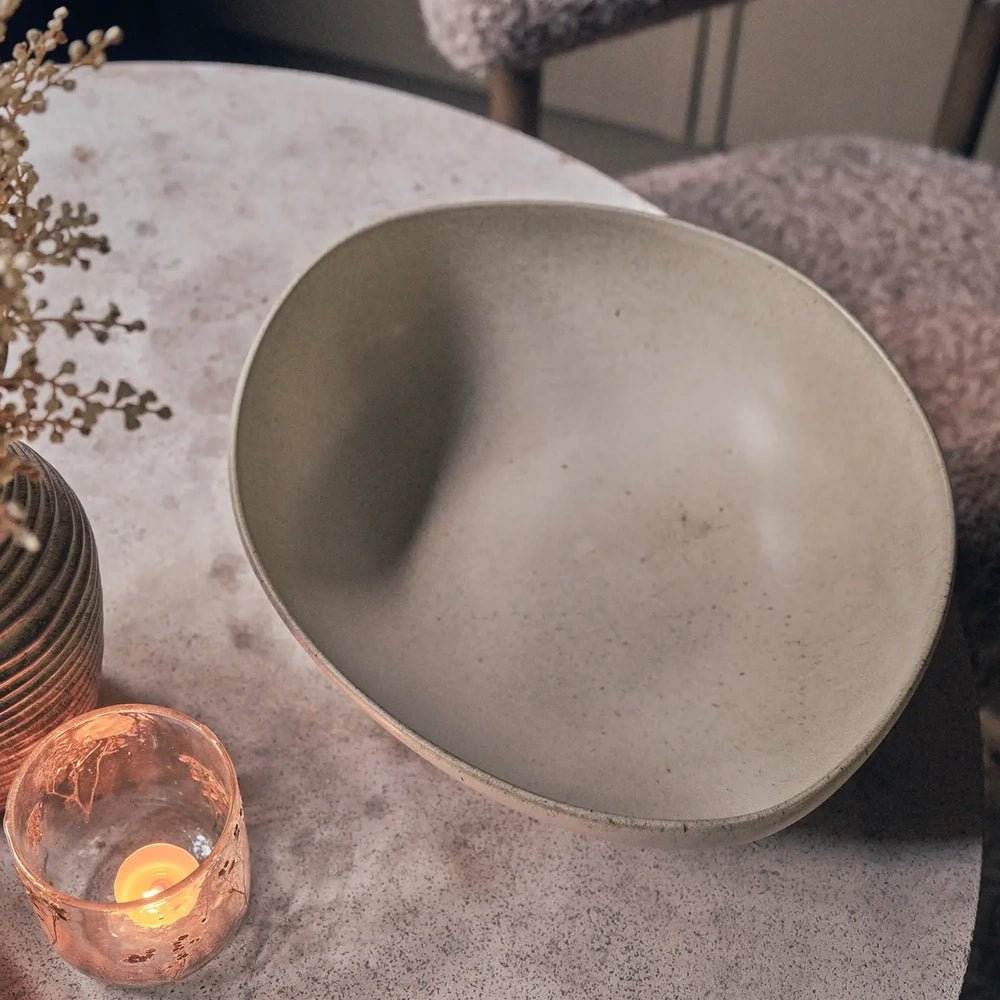 Alcott Serving Bowl viewed from above, revealing its broad curved interior, fine grey speckling and uneven rounded rim on a table beside a glowing candle.