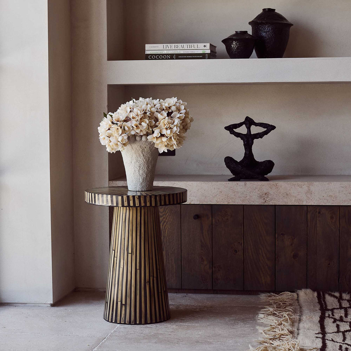 Decorative table with a vase of flowers and a sculpture in a room setting.