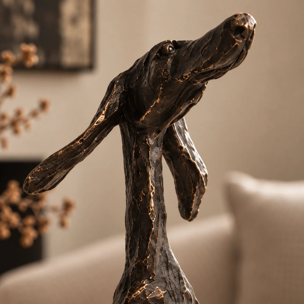 Arnie Sculpture standing on a console table, showing its dark angular dog silhouette beside stacked books, a lamp and textured decorative accessories.