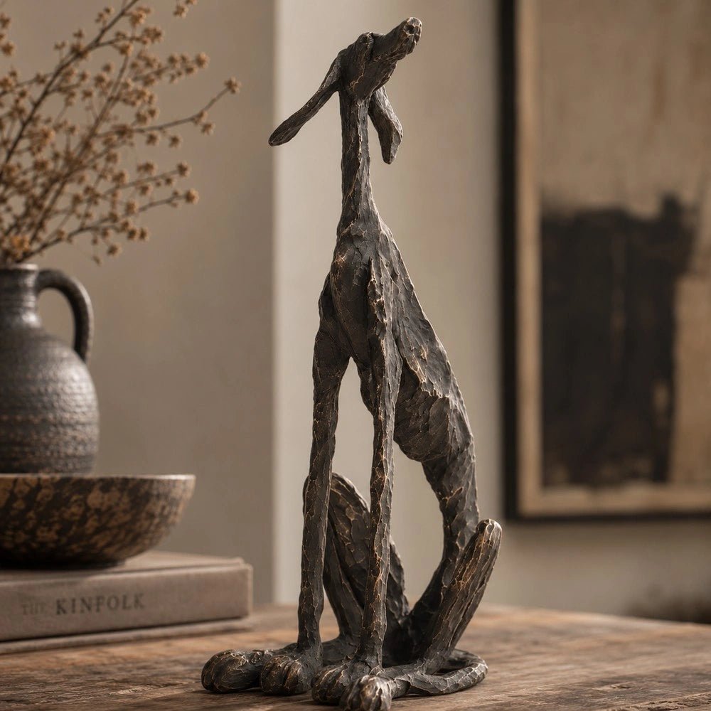 Arnie Sculpture with a dark angular dog form standing on a tabletop, styled beside stacked books, textured vessels and softly blurred neutral interior decor.