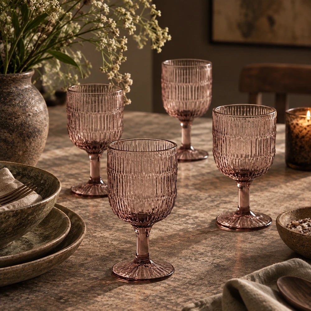 Aster Wine Glass, Blush set of four ribbed pink stemmed glasses arranged on a stone dining table with neutral ceramics, flowers and softly lit interior styling.