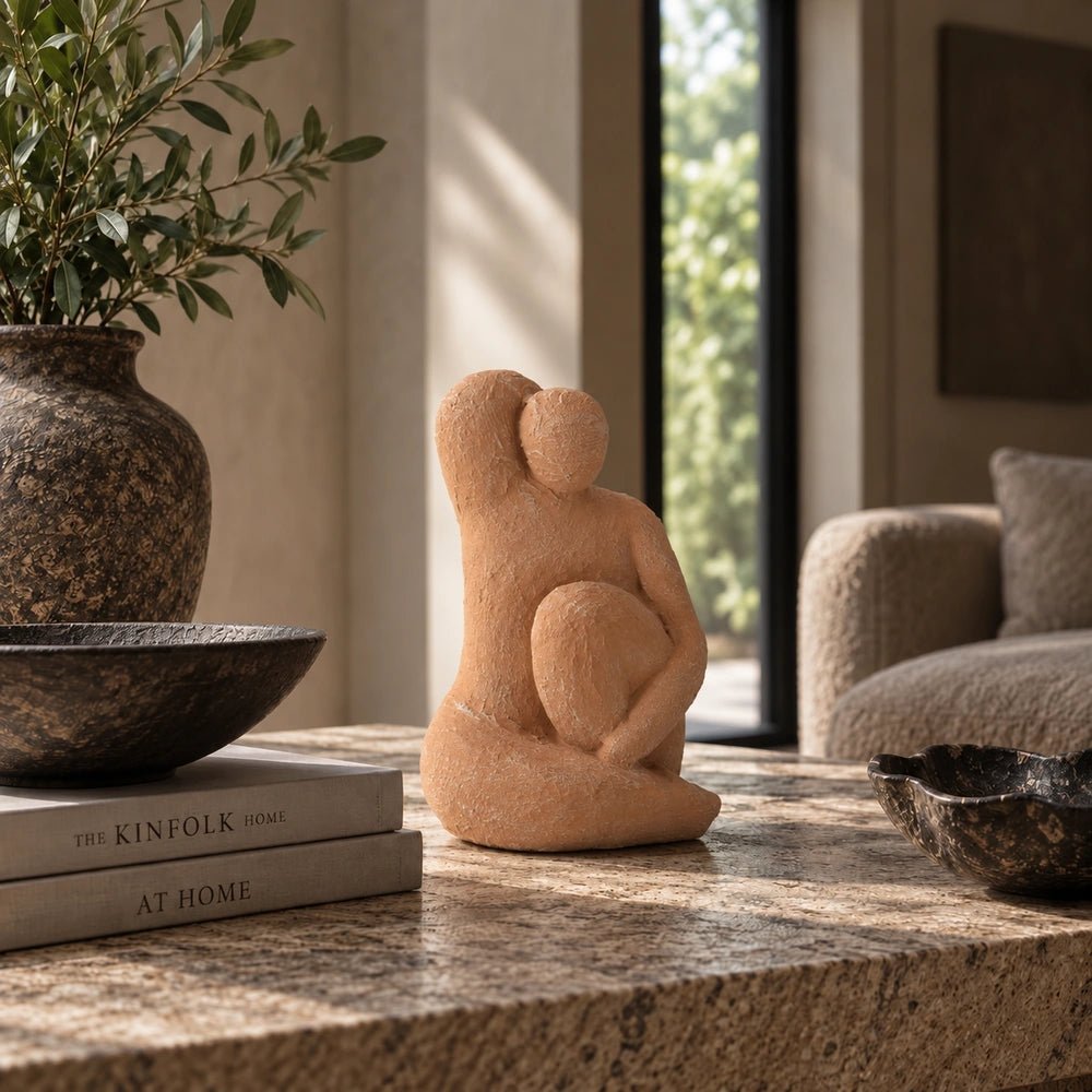 Aveline Figurative Sculpture in warm terracotta tones, displayed on a stone table beside stacked books and ceramics in a softly styled neutral interior.