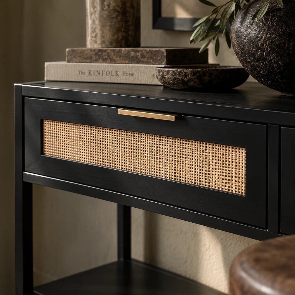 Bailey Wood Console Table close-up showing black framed drawers with woven cane panels and brass handles, styled with books, bowls and a dark textured vase.